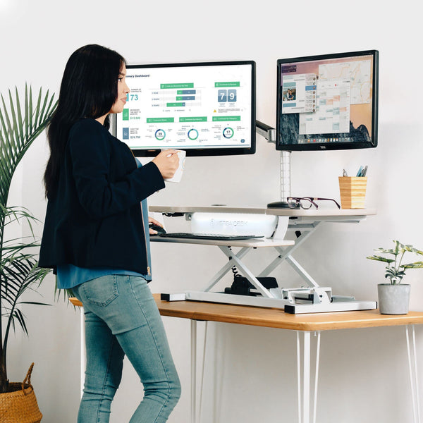 Height-adjustable standing desk raised to standing height in a home office, set up to ease low back pain